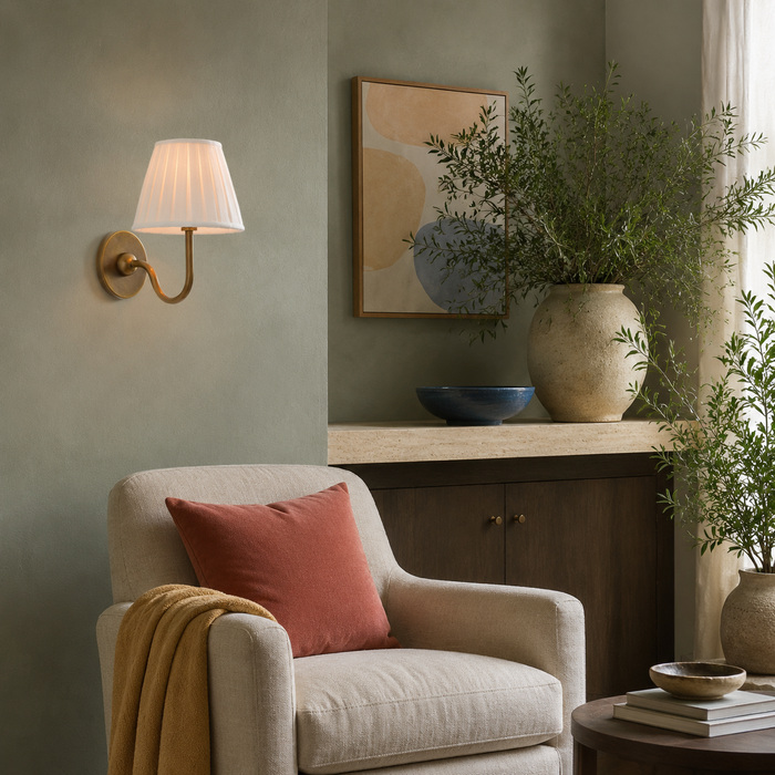 Een messing wandlamp gecombineerd met linnen, donker hout en natuurlijke planten in een saliegroene leeshoek.