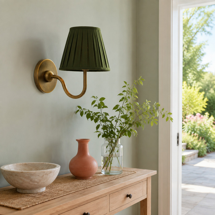 Groene, geplooide Baylor-wandlamp boven een licht eikenhouten console bij een lichte tuindeur.