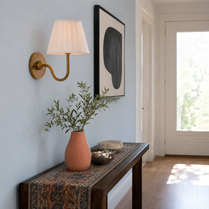Luvora wandlamp met plissépatroon boven een halconsole van walnotenhout met koraal- en chroomaccenten.