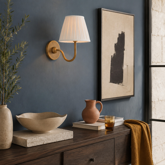 Wandlamp van getrommeld messing, gecombineerd met accenten van steen, donker hout en oker, tegen een blauwe muur.